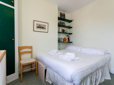 Bedroom with a double bed white linens wooden chair green shelves with books and framed pictures at Old Coastguard Cottages in Amble