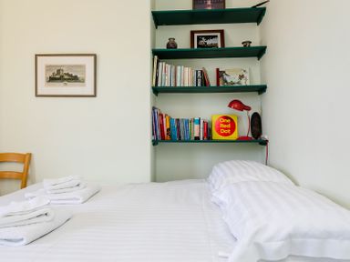 A bedroom with a bed with folded towels and a shelf with books and a red lamp at Old Coastguard Cottages in Amble
