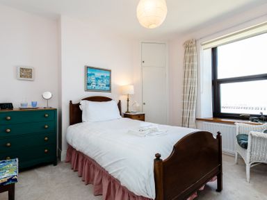 A bedroom with a wooden bed and white linens a green dresser and a window at Old Coastguard Cottages Amble