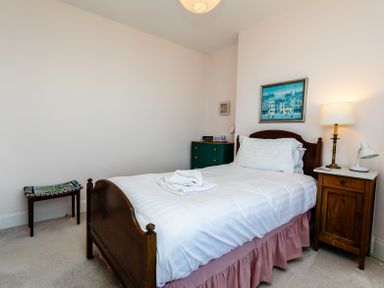 A bedroom with a wooden bed with white bedding and a pink bed skirt at Old Coastguard Cottages in Amble