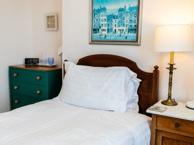 A bed with white pillows and a wooden headboard with a nightstand and lamp at Old Coastguard Cottages in Amble