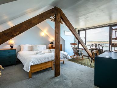 A bedroom with a bed side tables lamps rocking chairs and large window with water view at Old Coastguard Cottages in Amble