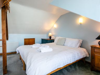 A bedroom with a double bed with white bedding and folded towels on top two bedside tables with lamps and a wooden post with hangers at Old Coastguard Cottages in Amble