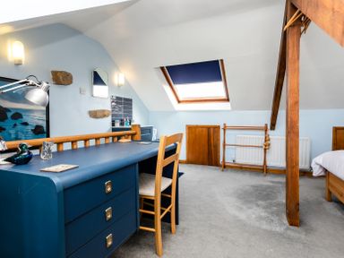 An attic bedroom with a blue desk and wooden chair under a skylight window at Old Coastguard Cottages in Amble