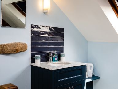 A bathroom sink with blue tiles and a mirror above at Old Coastguard Cottages in Amble