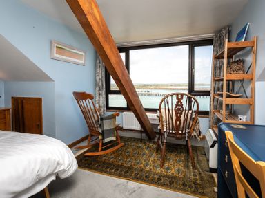 A room with two wooden chairs on a patterned rug by a window overlooking water at Old Coastguard Cottages Amble