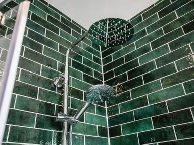 A shower with chrome shower heads and green tiled walls at Old Coastguard Cottages in Amble