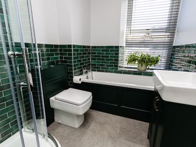 A bathroom with a shower, toilet, bathtub, sink, and a plant on the windowsill at Old Coastguard Cottages in Amble