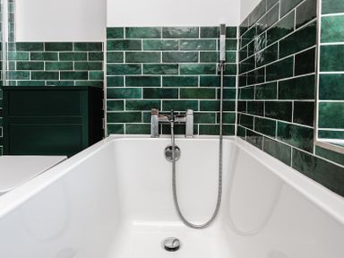 A bathtub with chrome fixtures and green tiled walls in a bathroom at Old Coastguard Cottages in Amble