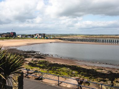 A coastal scene with a sandy beach a wooden pier and buildings in the distance at Old Coastguard Cottages Amble