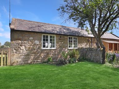 An outdoor view of a stone cottage with a garden at Plumtree Cottage in Alnmouth