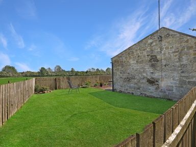 A garden with grass, a chair, and flower pots at Plumtree Cottage in Alnmouth