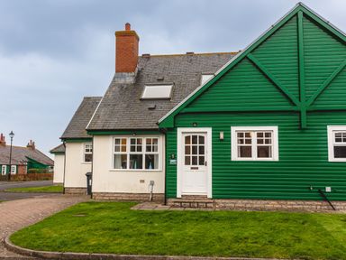 A house with white walls and a green wooden extension with windows and a door at Armstrong Cottages No30 in Bamburgh