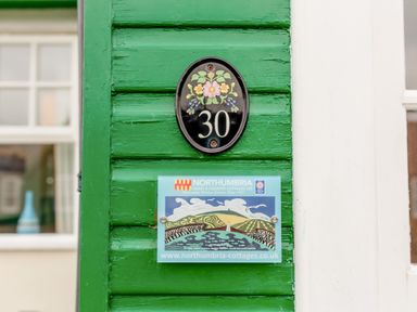 Green wooden wall with house number 30 and a northumbria cottages sign at Armstrong Cottages No30 in Bamburgh