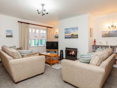 A living room with two beige sofas a wooden coffee table a fireplace and a television at Armstrong Cottages No30 in Bamburgh