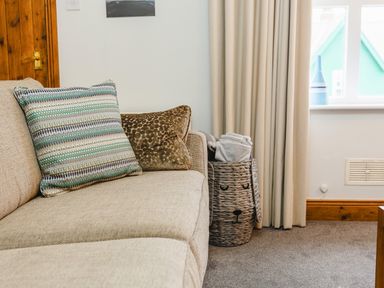A beige sofa with two cushions next to a woven basket holding folded blankets by a window at Armstrong Cottages No30 in Bamburgh