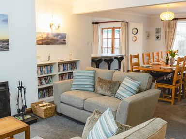 A living room with a sofa and pillows a bookshelf and a dining table with chairs at Armstrong Cottages No30 in Bamburgh