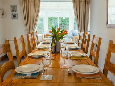 A dining room with a set wooden table with plates glasses and flowers at Armstrong Cottages No30 in Bamburgh