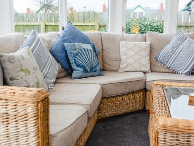 A corner sofa with patterned cushions and a glass-topped wicker coffee table at Armstrong Cottages No30 in Bamburgh