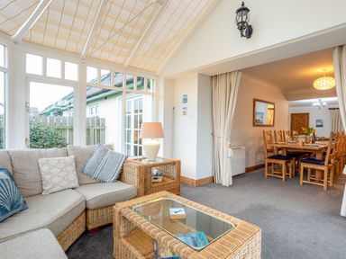 A seating area with a wicker sofa and glass table adjacent to a dining room with a wooden table and chairs at Armstrong Cottages No30 Bamburgh