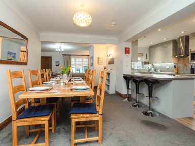 A dining room with a wooden table and chairs set for a meal next to a kitchen with bar stools at Armstrong Cottages No30 in Bamburgh