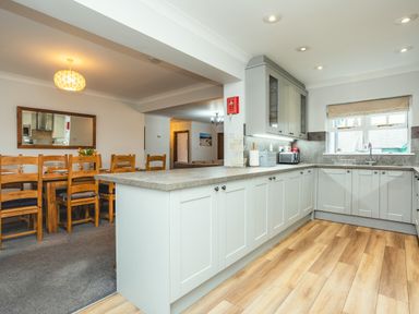 A kitchen with white cabinets and wooden flooring connected to a dining area with a wooden table and chairs at Armstrong Cottages No30 Bamburgh