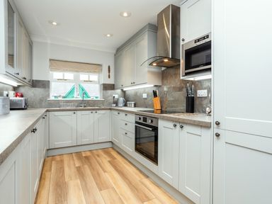 A kitchen with white cabinets wooden floor and stainless steel appliances at Armstrong Cottages No30 in Bamburgh