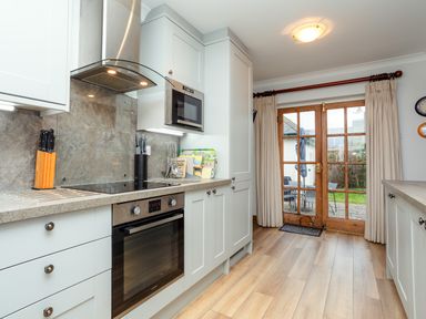 A kitchen with white cabinets a stove oven microwave and wooden doors leading outside at Armstrong Cottages No30 Bamburgh