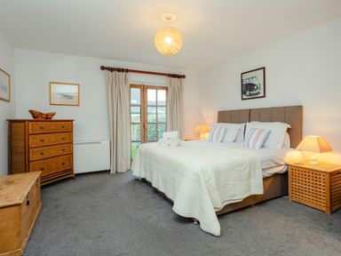 A bedroom with a bed a wicker chest a dresser and two lamps at Armstrong Cottages No30 Bamburgh
