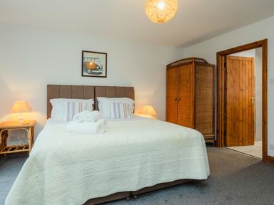 A bedroom with a double bed bedside tables with lamps a wooden wardrobe and an open door at Armstrong Cottages No30 in Bamburgh