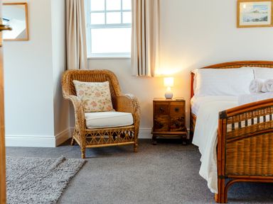 A bedroom with a wicker chair a bedside table with a lamp and a bed with rolled towels at Armstrong Cottages No30 in Bamburgh