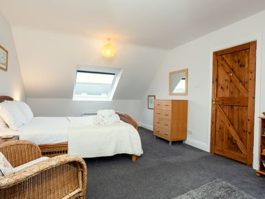 A bedroom with a bed towels wicker chair wooden dresser and wooden door at Armstrong Cottages No30 in Bamburgh