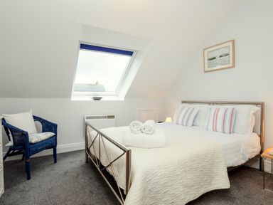 A bedroom with a bed and striped pillows a blue chair and a skylight window at Armstrong Cottages No30 in Bamburgh