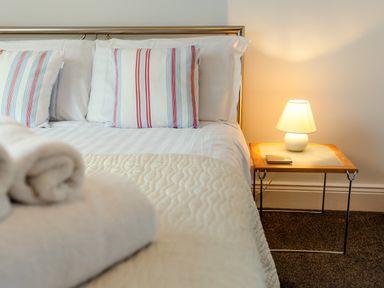 A bed with striped pillows and white linens next to a nightstand with a lamp at Armstrong Cottages No30 in Bamburgh