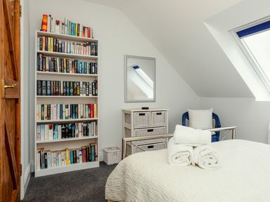 A bedroom with a bed and folded towels a bookshelf a wicker drawer unit and a window at Armstrong Cottages No30 Bamburgh