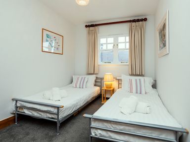 A bedroom with two single beds a lamp on a small wooden table between them and framed pictures on the walls at Armstrong Cottages No30 in Bamburgh