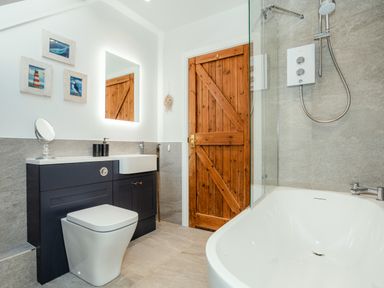 A bathroom with a bathtub shower toilet wooden door and wall art at Armstrong Cottages No30 in Bamburgh
