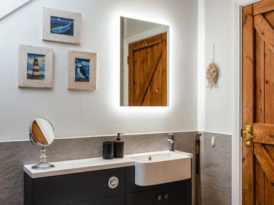 A bathroom sink with mirror above and framed pictures on wall at Armstrong Cottages No30 Bamburgh