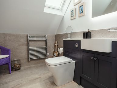 A bathroom with a toilet sink cabinet towel rack and a purple chair at Armstrong Cottages No30 in Bamburgh