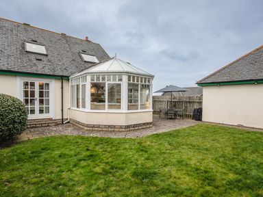 A garden with grass and a patio area with outdoor furniture and umbrella next to a house with conservatory at Armstrong Cottages No30 Bamburgh