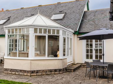 A conservatory attached to a house with a patio table chairs and an umbrella at Armstrong Cottages No30 in Bamburgh