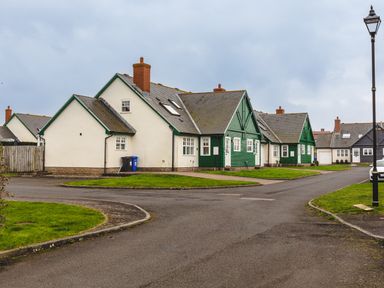 A street view of houses with green and white exteriors and lawns at Armstrong Cottages No30 in Bamburgh