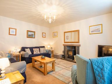 A living room with sofas a coffee table a fireplace and framed pictures on the walls at Lobster Pot Cottage in Seahouses