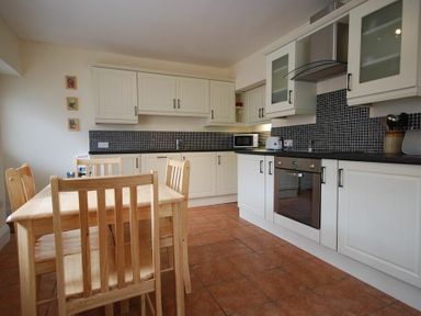 A kitchen with wooden dining table and chairs and white cabinets at Lobster Pot Cottage in Seahouses