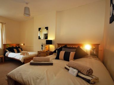 A bedroom with two beds each with folded towels a bedside table with a lamp and mirror on the wall at Lobster Pot Cottage in Seahouses
