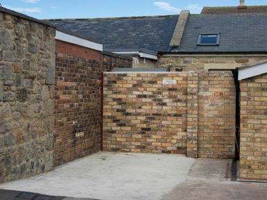 A small enclosed area with brick walls and a concrete floor with a sign reading private no parking at Lobster Pot Cottage in Seahouses