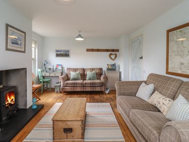 A living room with two checkered sofas a wooden chest coffee table a desk with chair and a fireplace at Beachward in Embleton