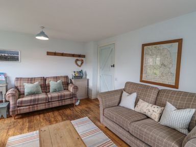 A living room with two plaid sofas wooden floor and a framed map on the wall at Beachward in Embleton