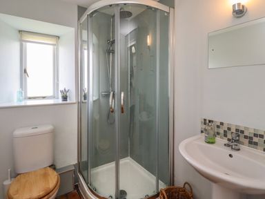 A bathroom with a corner shower enclosure toilet with wooden seat a sink a mirror and a window at Beachward in Embleton