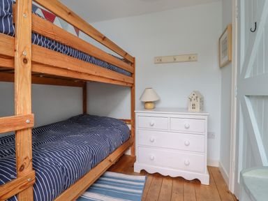 A bedroom with wooden bunk beds a white chest of drawers and a lamp at Beachward in Embleton